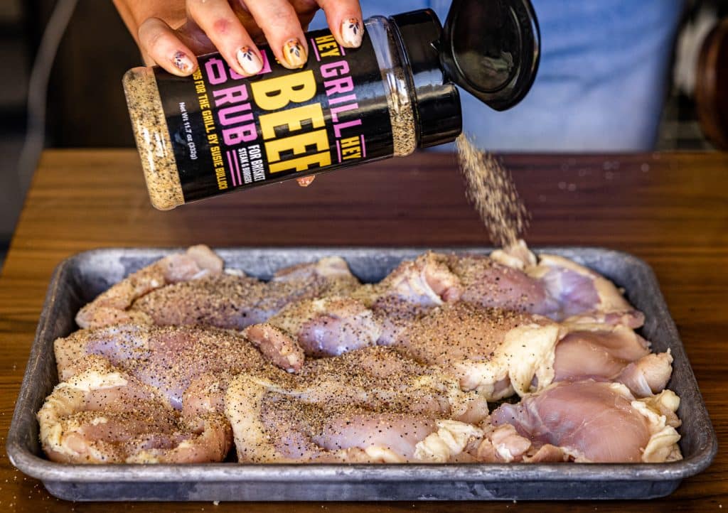 Beef Rub being sprinkled on chicken thighs.