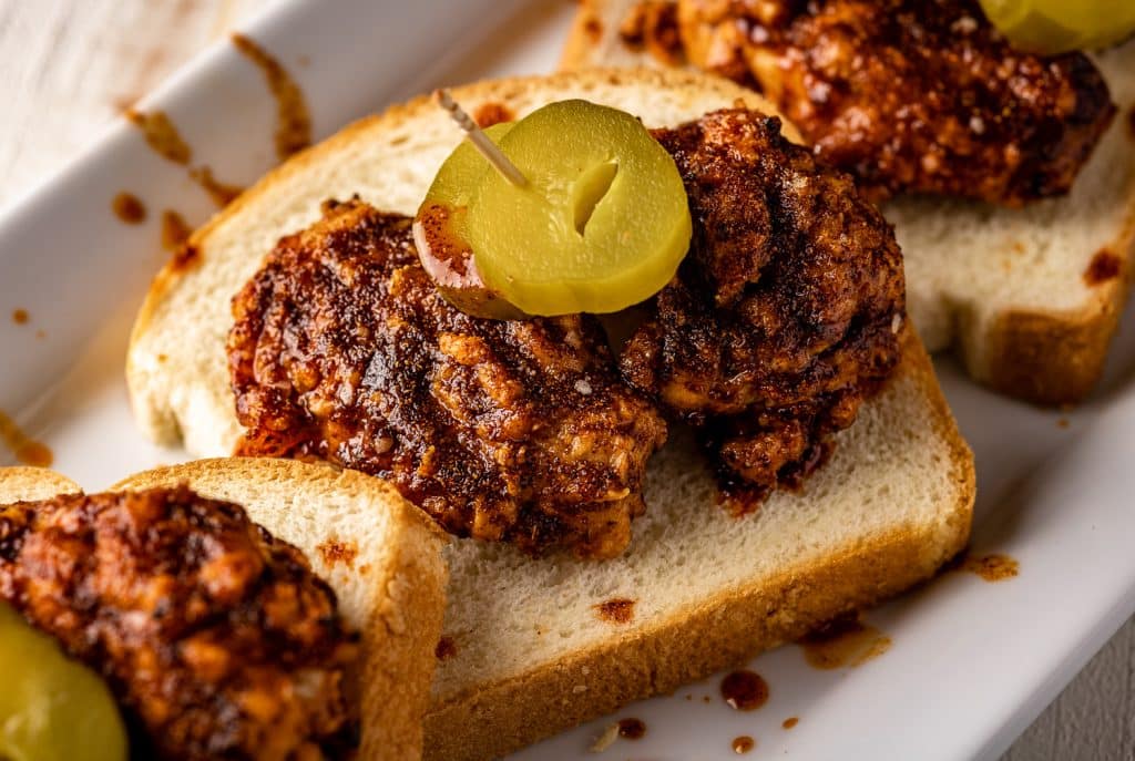 Grilled Nashville hot wings on a slice of bread topped with pickles.