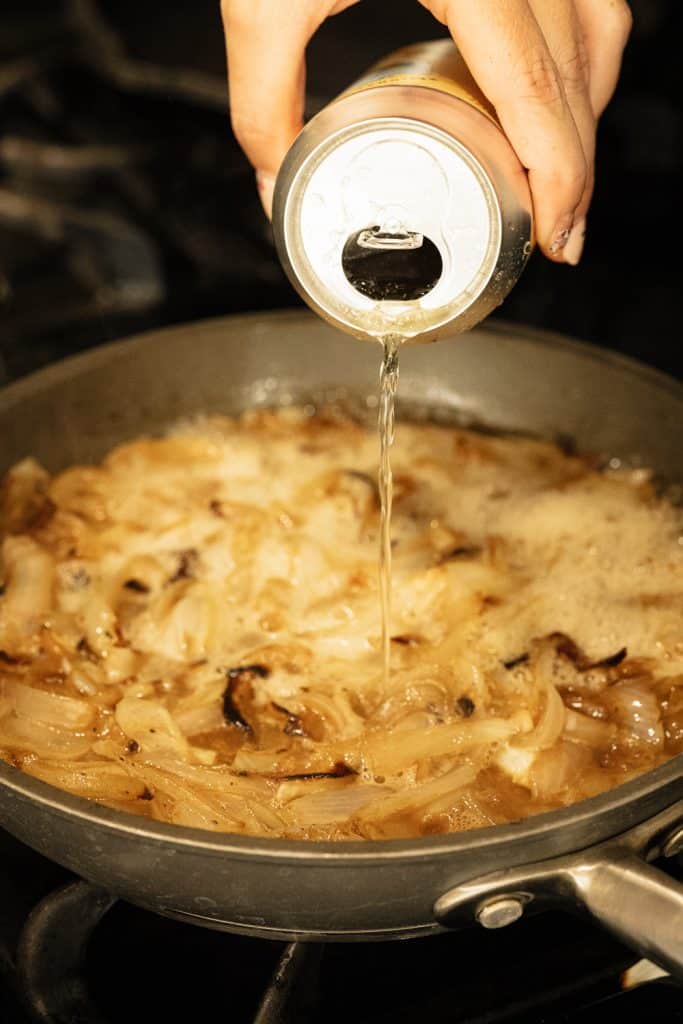 Beer being poured over a skillet of sliced onions.