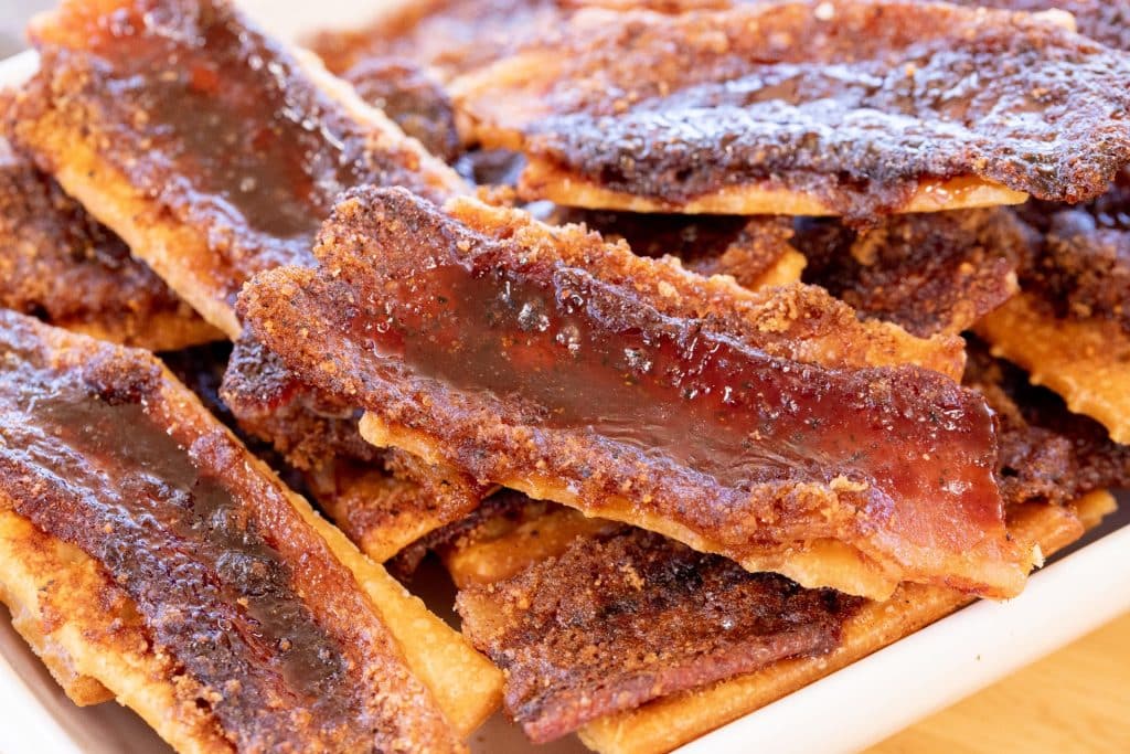 Pile of candied bacon covered crackers on a serving dish.