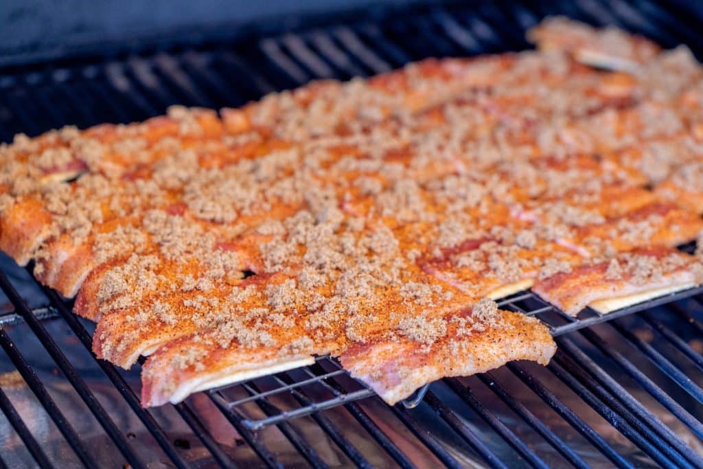 Club crackers covered with bacon and brown sugar on the grill grates of a smoker.