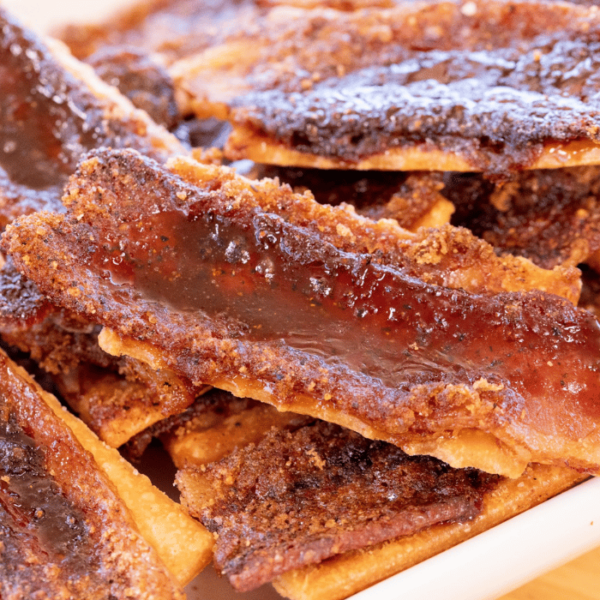 Pile of candied bacon covered crackers on a serving dish.