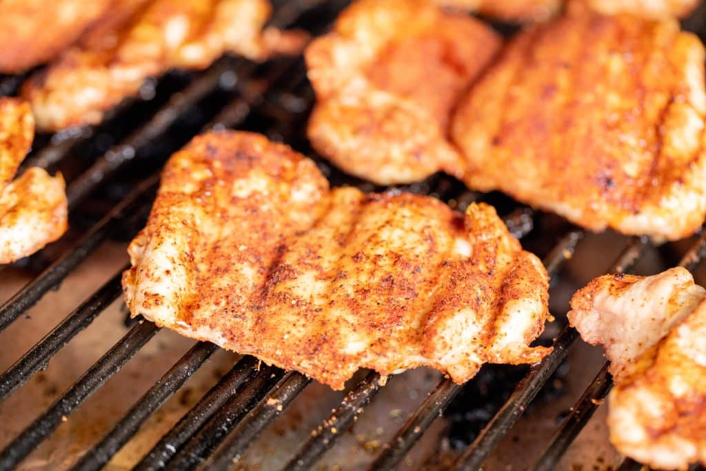 Seasoned chicken thighs on the grill grates of a smoker.