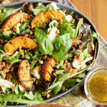 Grilled peach salad in a large serving dish next to a small jar of dressing.