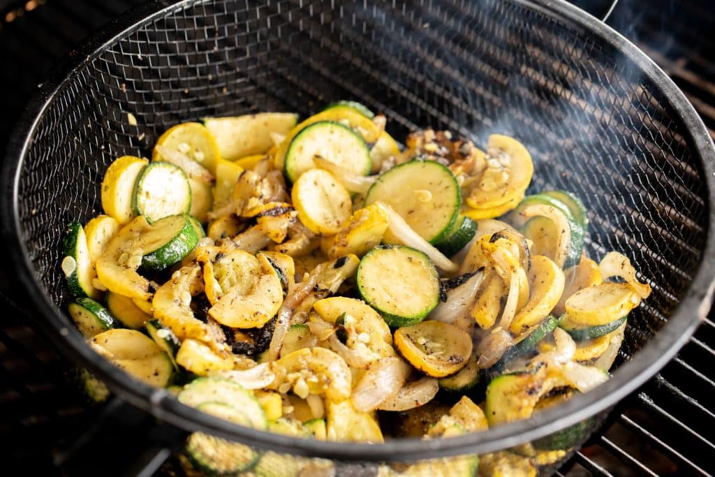 Seasoned zucchini and squash in a grill basket on the grill.