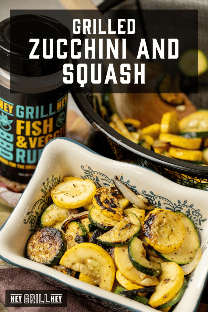 Grilled zucchini and squash in a serving dish next to a bottle of Hey Grill Hey Fish & Veggie Rub with text overlay - Grilled Zucchini and Squash.