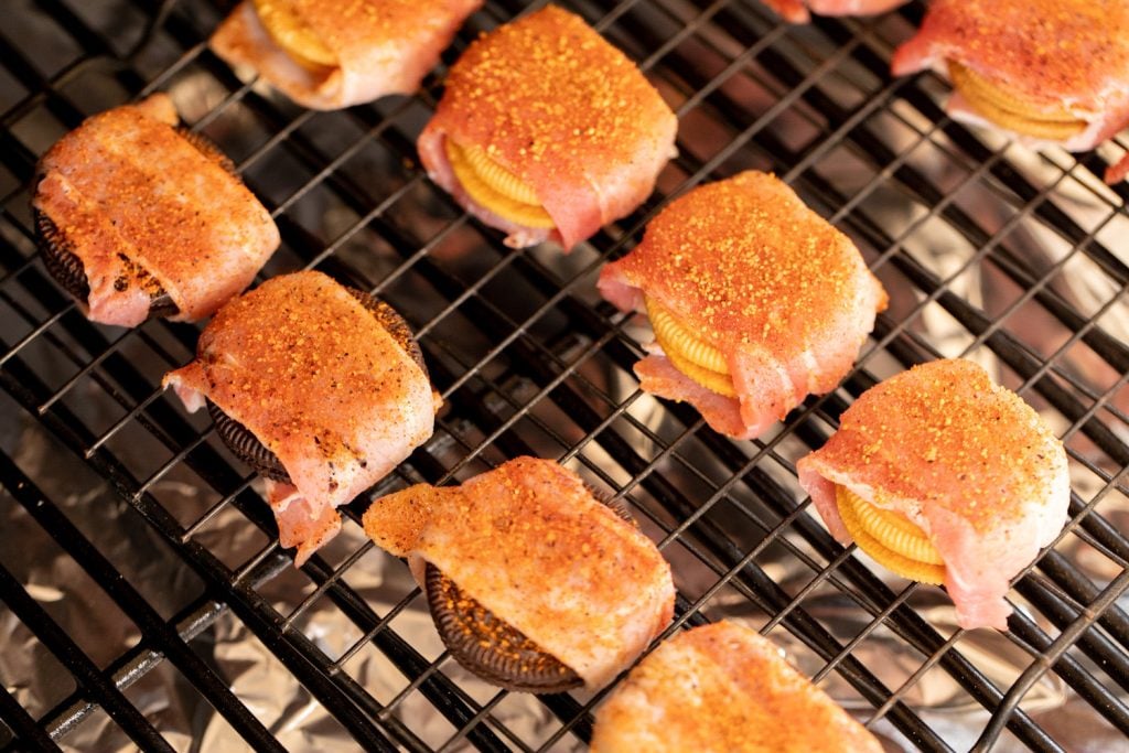 Bacon wrapped oreos on the grill grates of a smoker.