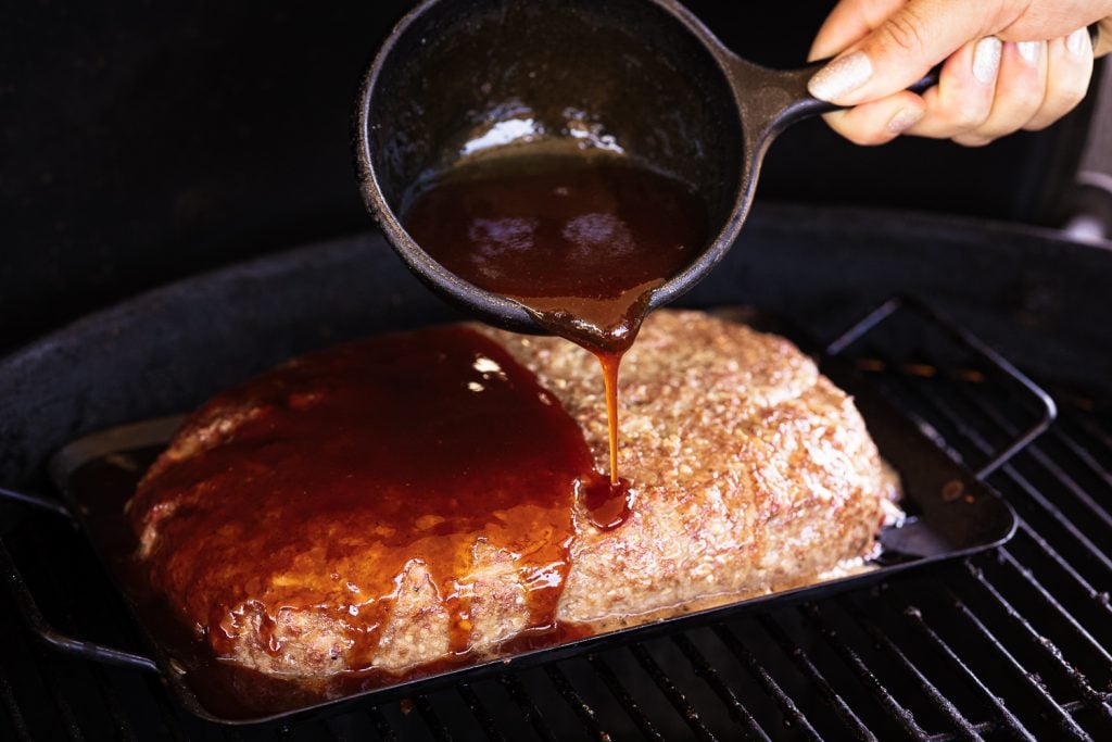 BBQ sauce glaze being poured on meatloaf on the grill.
