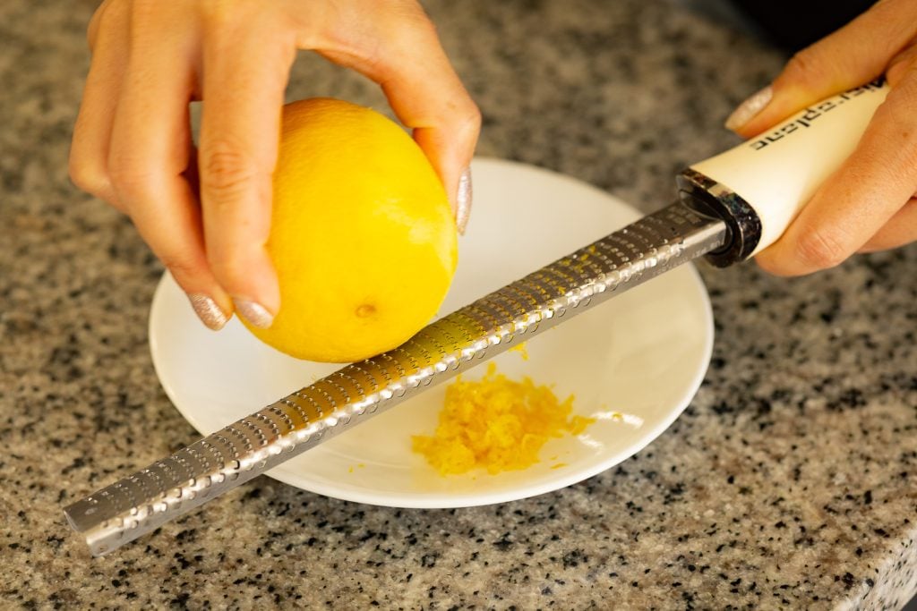 Lemon zest being grated onto a white plate.