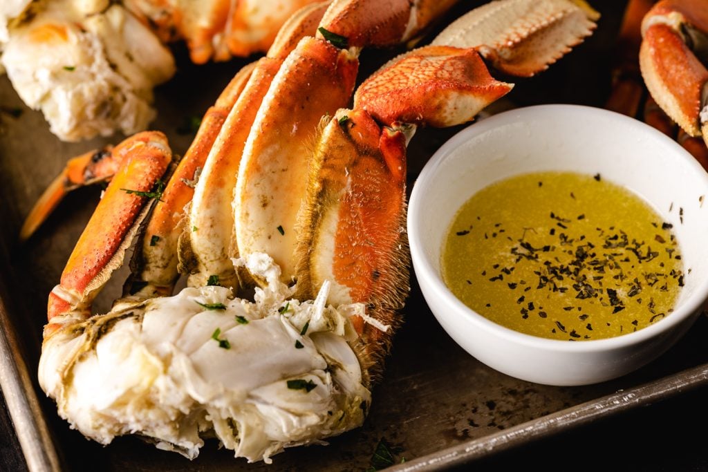 Smoked crab legs on a large serving platter next to seasoned BBQ butter dipping sauce.