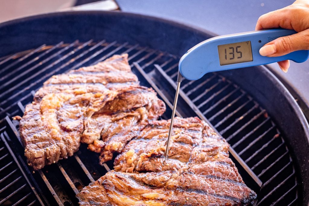 Chuck steaks on the grill with an instant-read thermometer reading 135 degrees F.