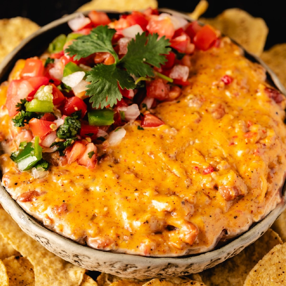 A bowl of smoked queso topped with fresh pico de gallo sitting on a bed of tortilla chips.