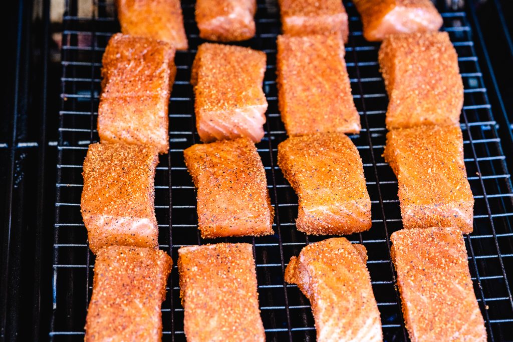 Cubed and seasoned salmon on the grill grates of the smoker.