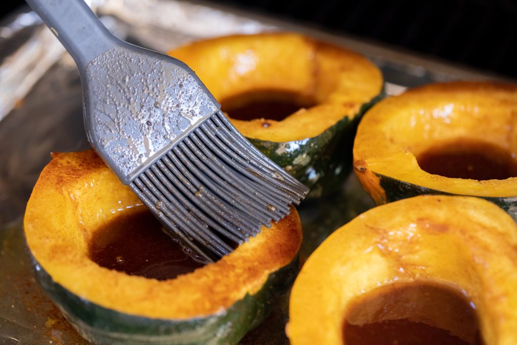 Acorn squash halves being basted with brown sugar butter.