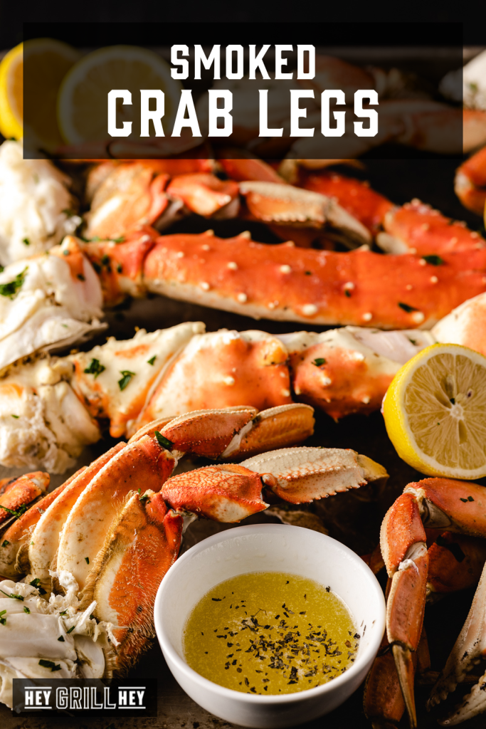 Smoked crab legs on a large serving platter next to seasoned BBQ butter dipping sauce with text overlay - Smoked Crab Legs.