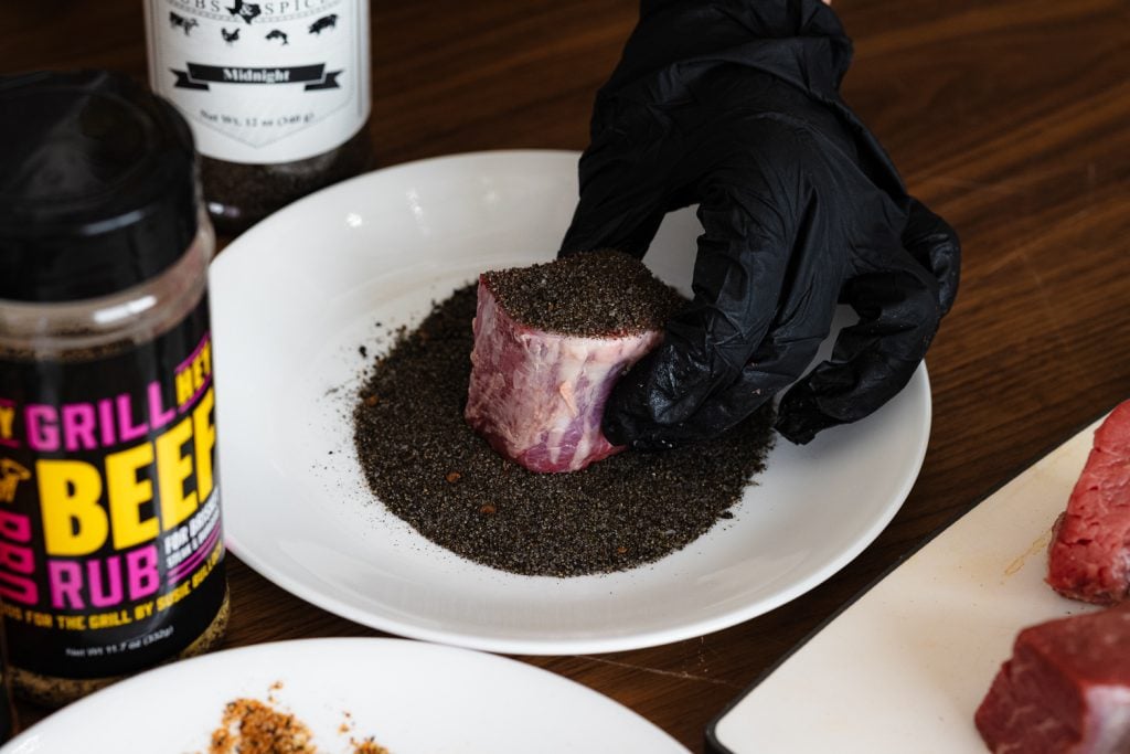 Steak bite being dipped into an activated charcoal BBQ rub.
