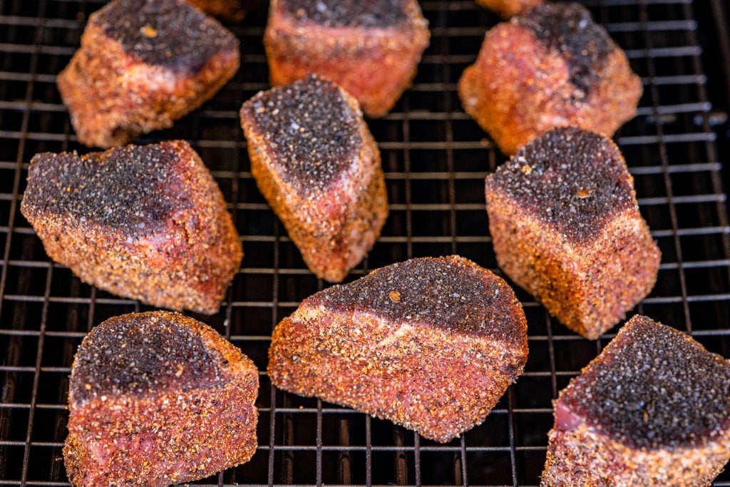 Seasoned steak bites on the grill grates of a smoker.