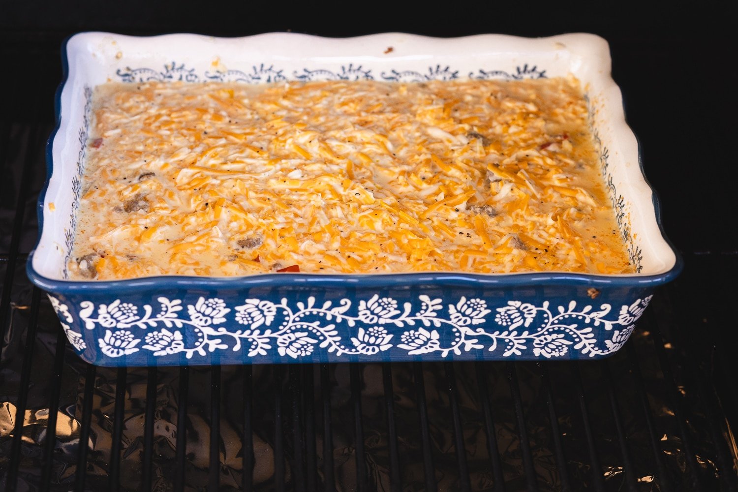 Casserole dish filled with eggs, cheese, sausage and hashbrowns on a smoker.