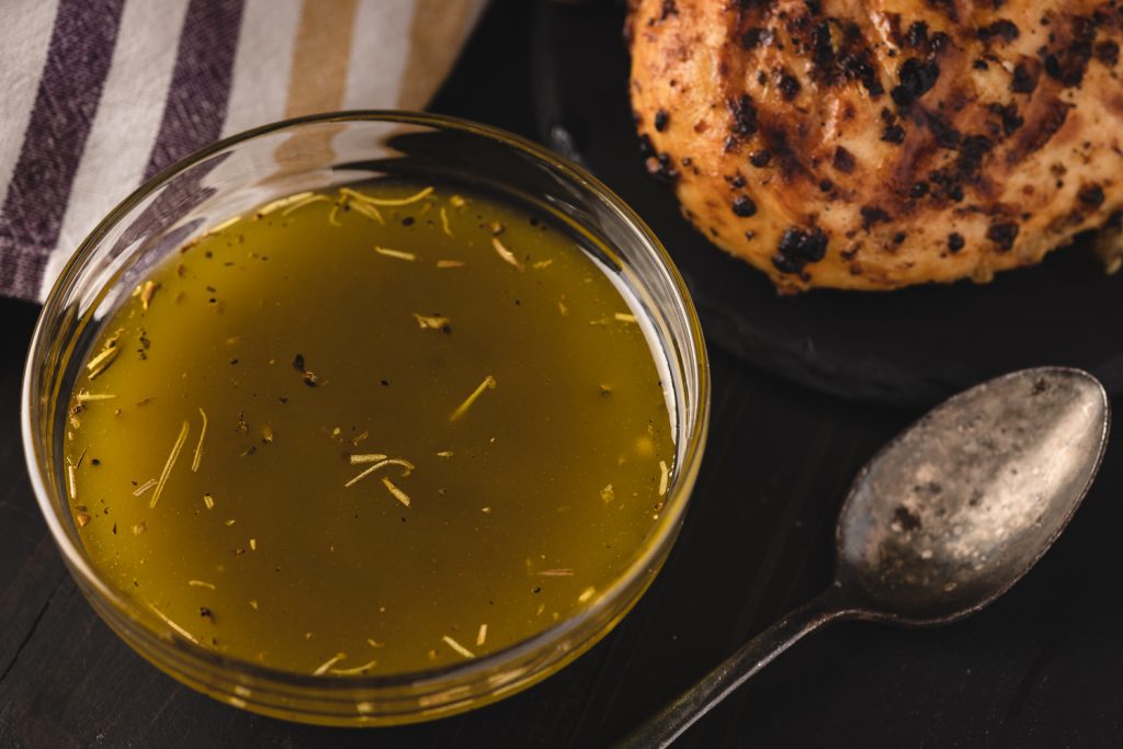 Grilled chicken marinade in a glass bowl next to a grilled chicken breast.