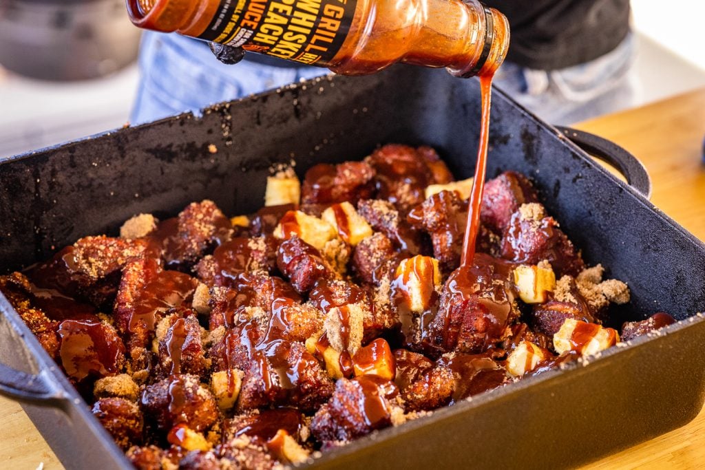 Whiskey Peach BBQ sauce being poured into a pan of pork shoulder burnt ends.