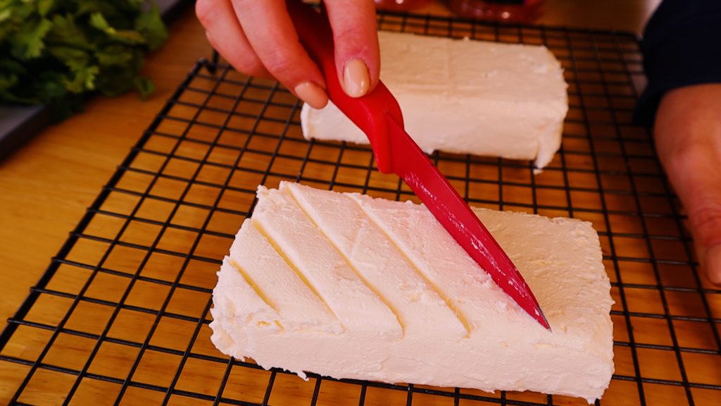 Two blocks of cream cheese being scored with a knife.