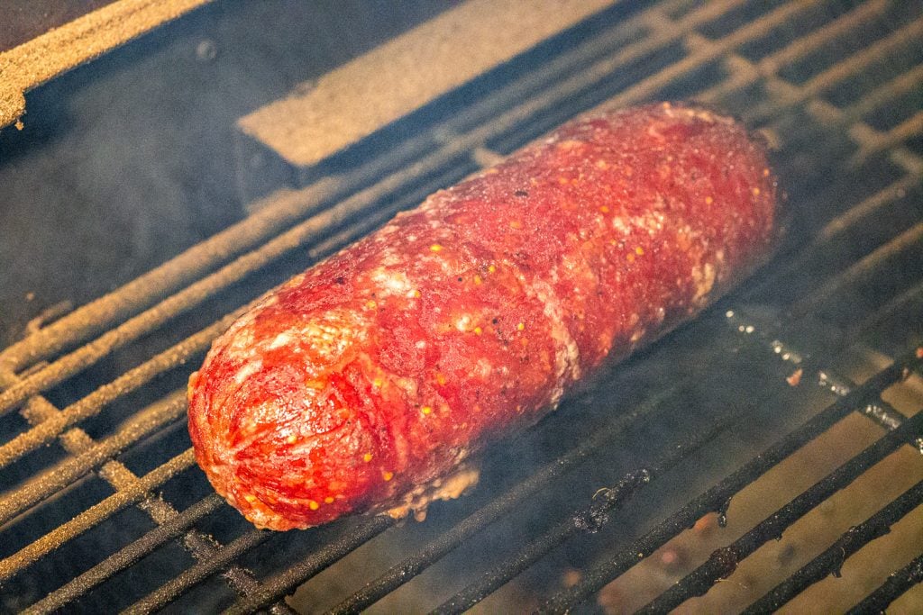 Summer sausage loaf on the grill grates of a smoker.