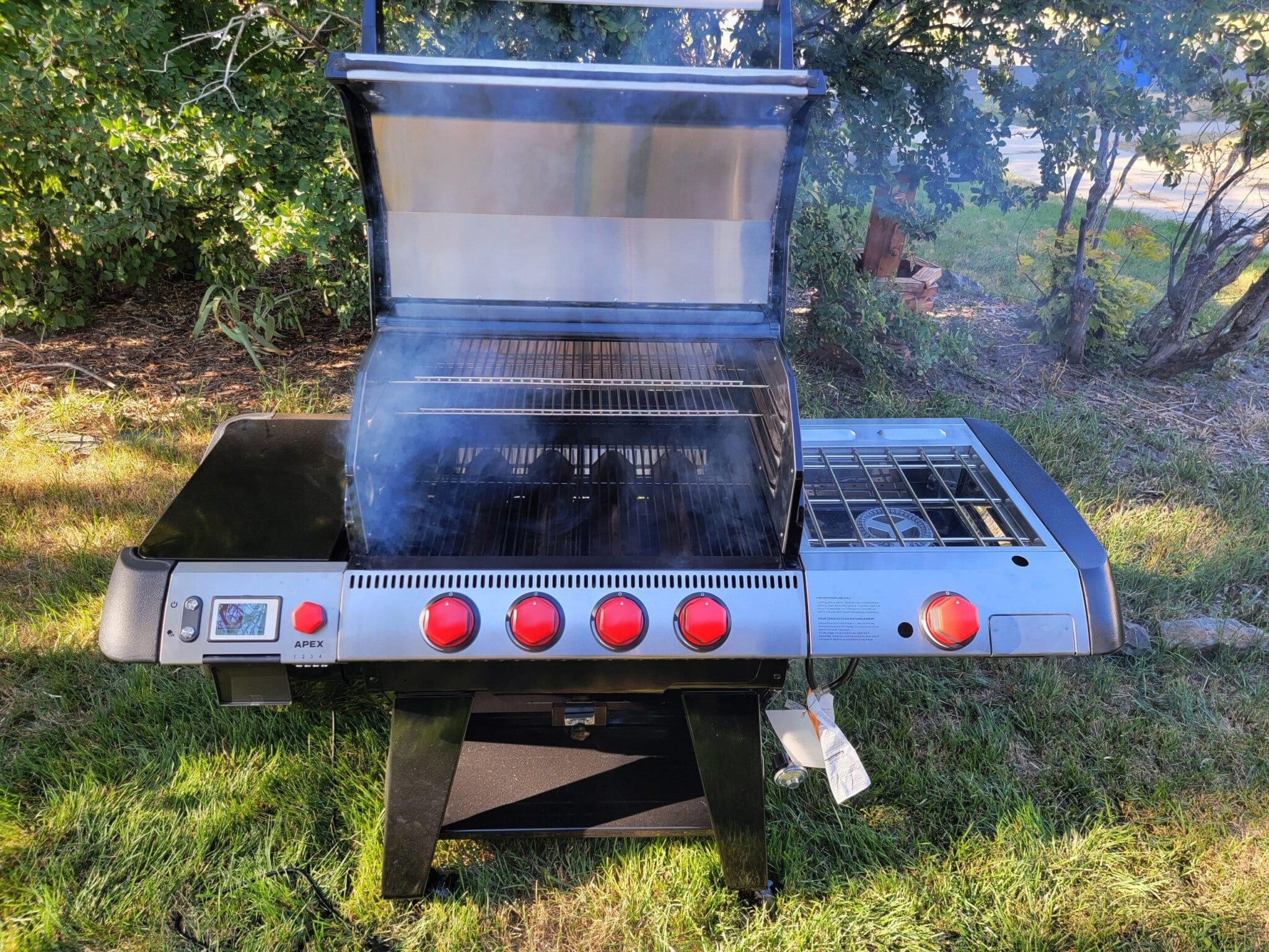 Apex grill on grass with lid open and smoke coming out