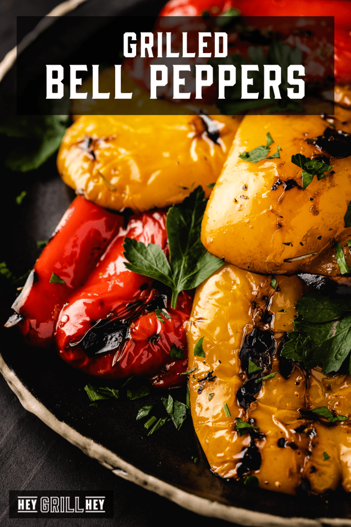 Grilled red, orange, and yellow peppers on a black serving dish with text overlay - Grilled Bell Peppers.