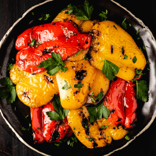 Grilled red, orange, and yellow peppers on a black serving dish.
