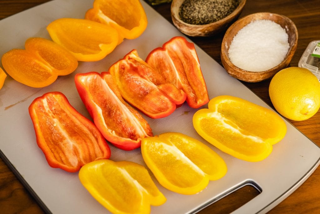 Sliced orange, red, and yellow bell peppers on a cutting board.