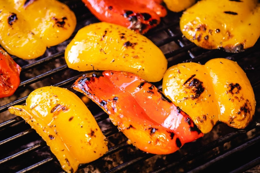 Sliced bell peppers on the grill grates of a grill.