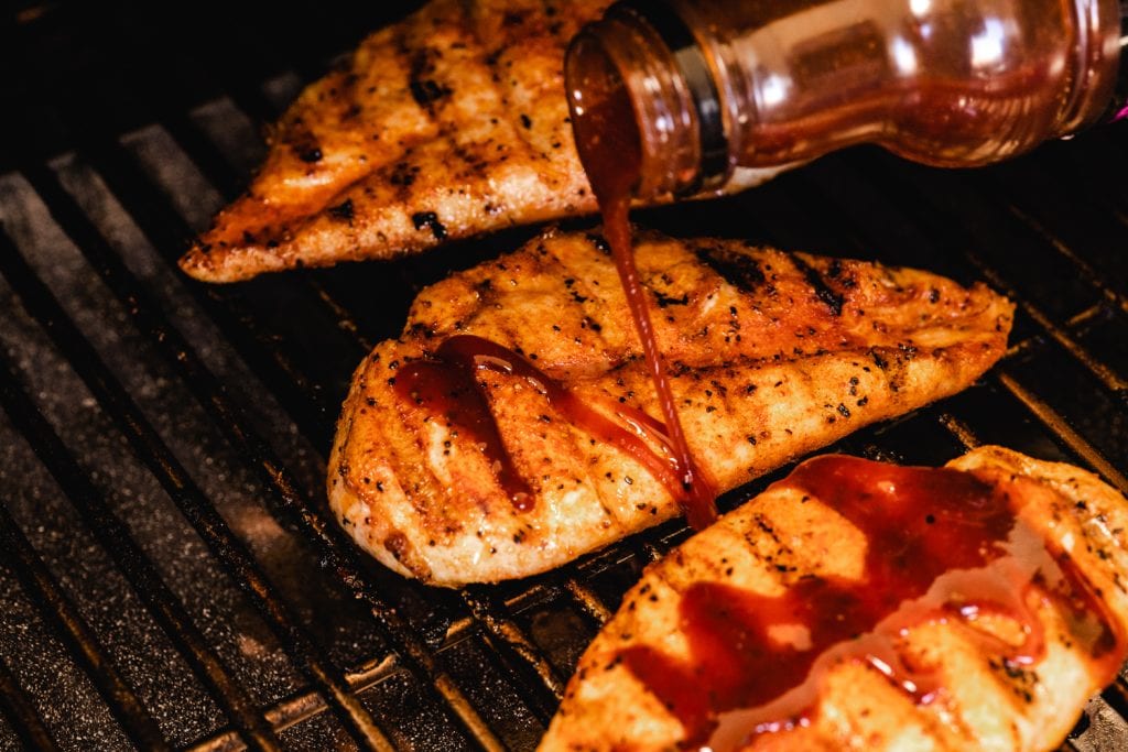 Chicken breast on the grill being drizzled with BBQ sauce.