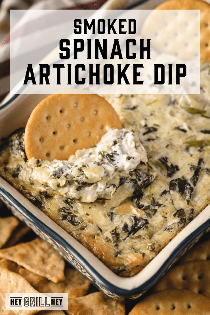 Cracker in a dish of smoked spinach artichoke dip with text overlay - Smoked Spinach Artichoke Dip.
