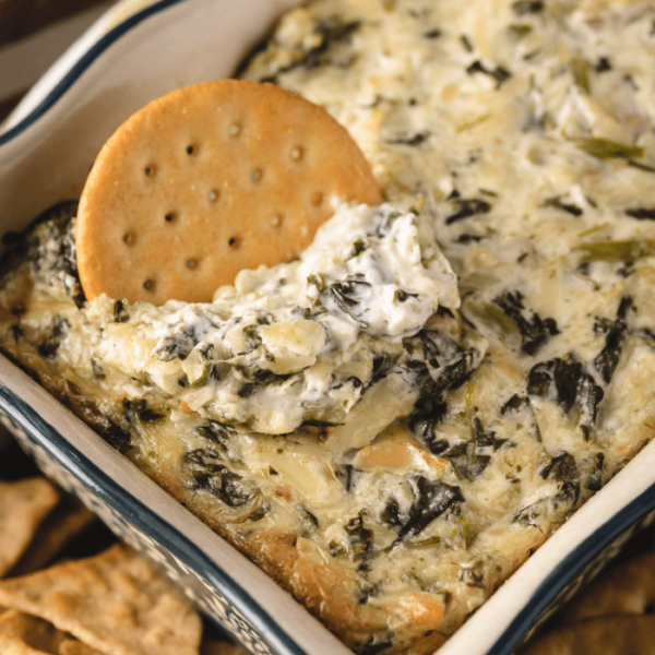 Cracker in a dish of smoked spinach artichoke dip.