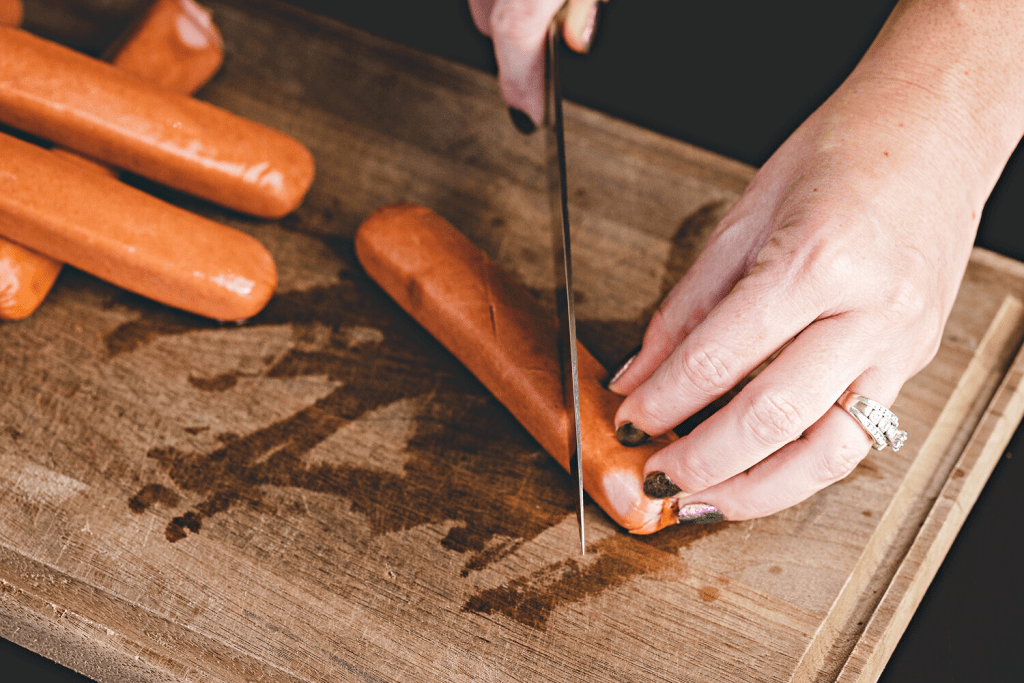 Hot dogs being scored on a wooden cutting board.