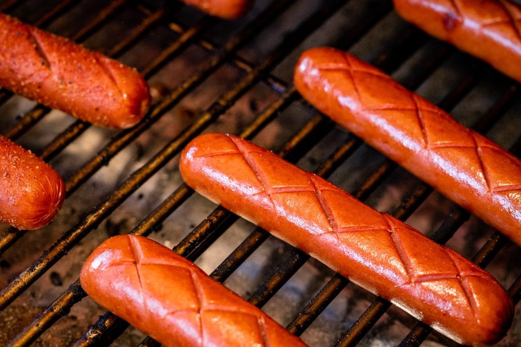 Hot dogs lined up on the grill grates of a smoker.
