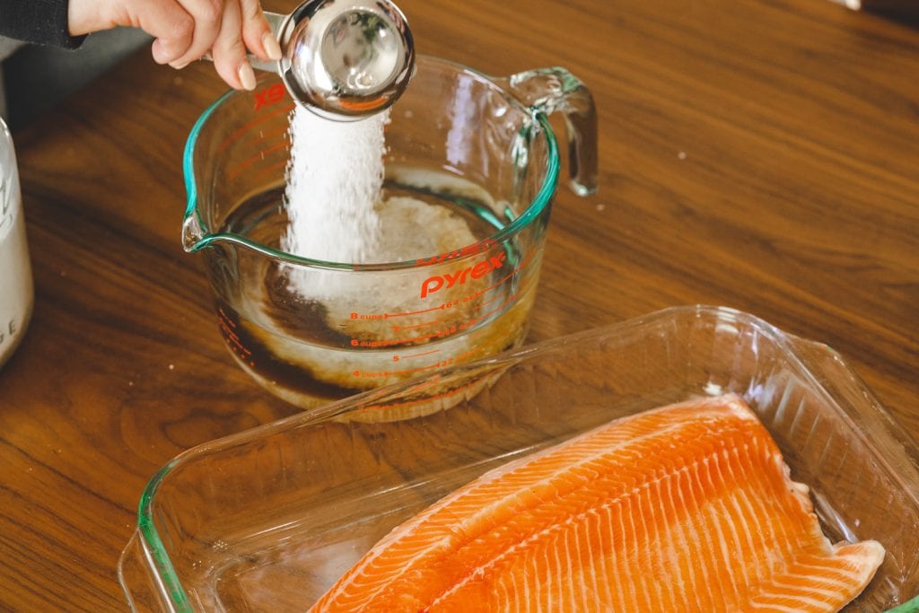 Salt being poured into a glass dish for smoked salmon brine.