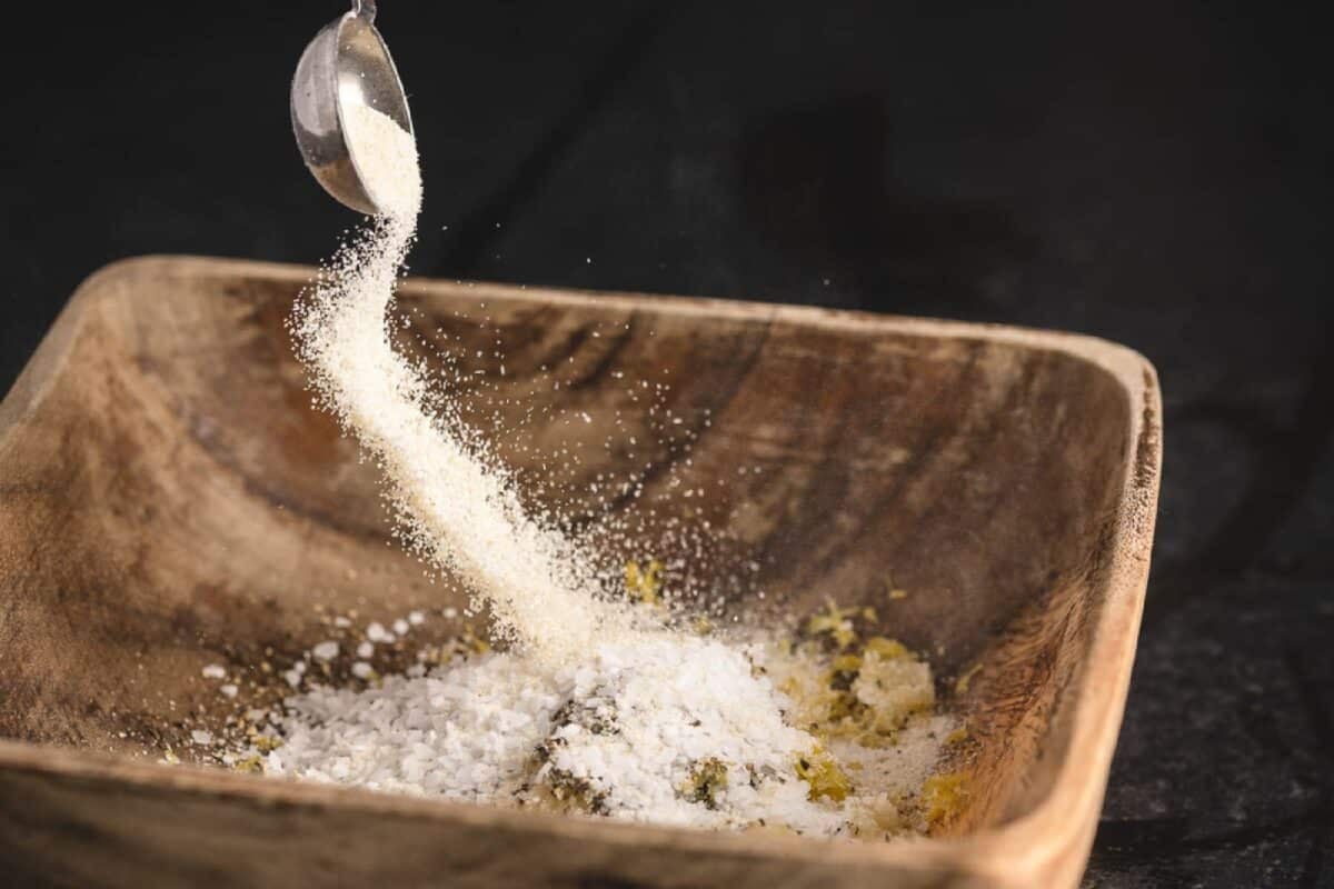 Salt being poured into wooden dish from metal measuring spoon.