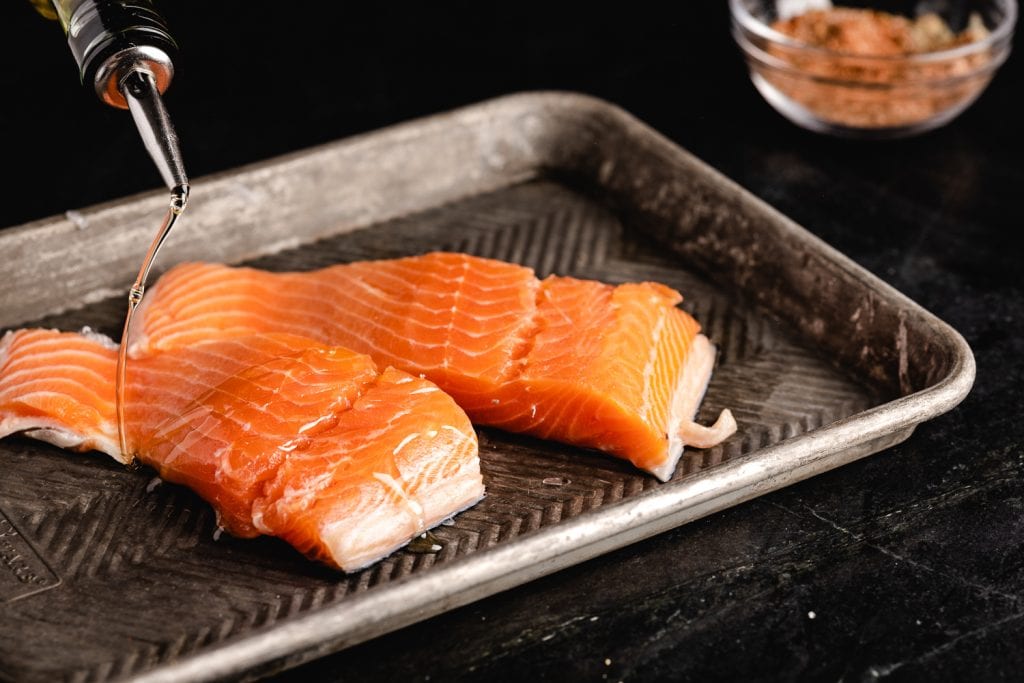 Two salmon filets being drizzled with olive oil.