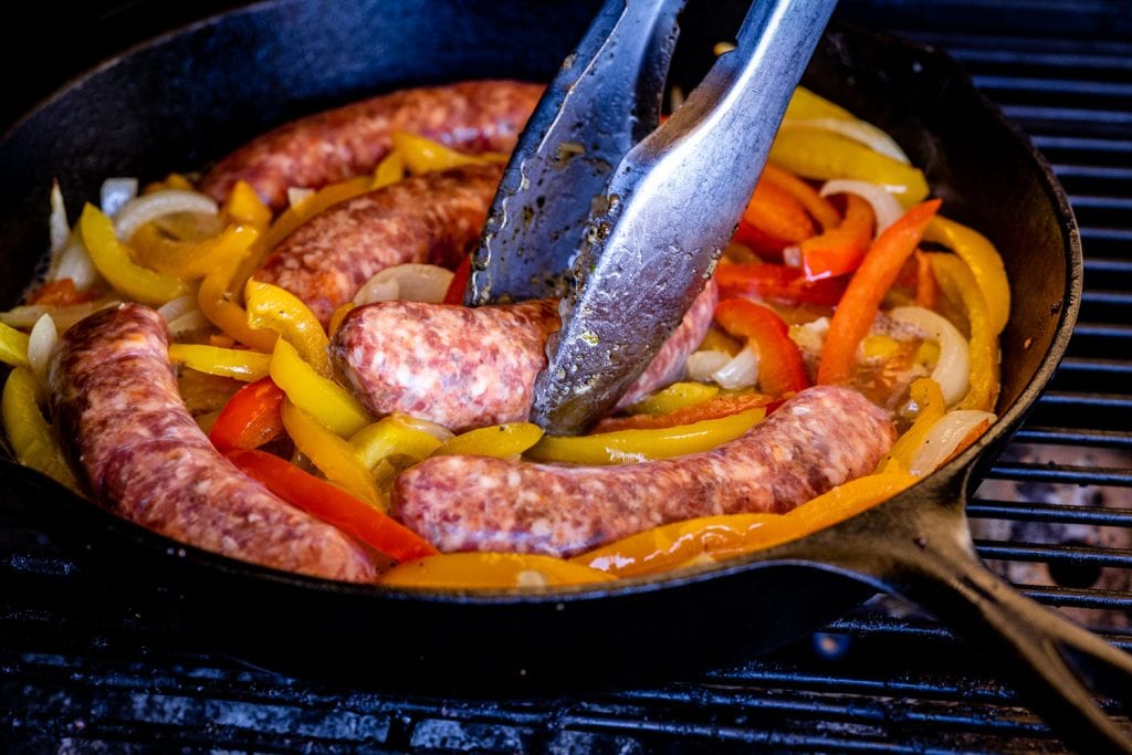 Italian sausage being added to a skillet of sliced bell peppers.