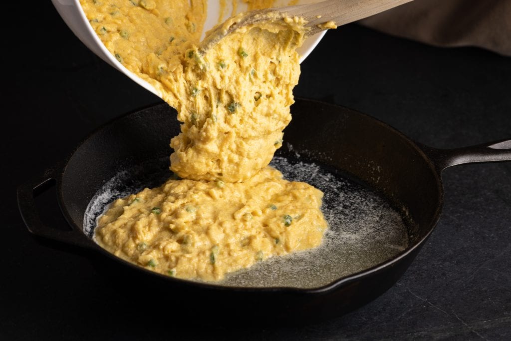 Cornbread batter being added to a cast iron skillet.