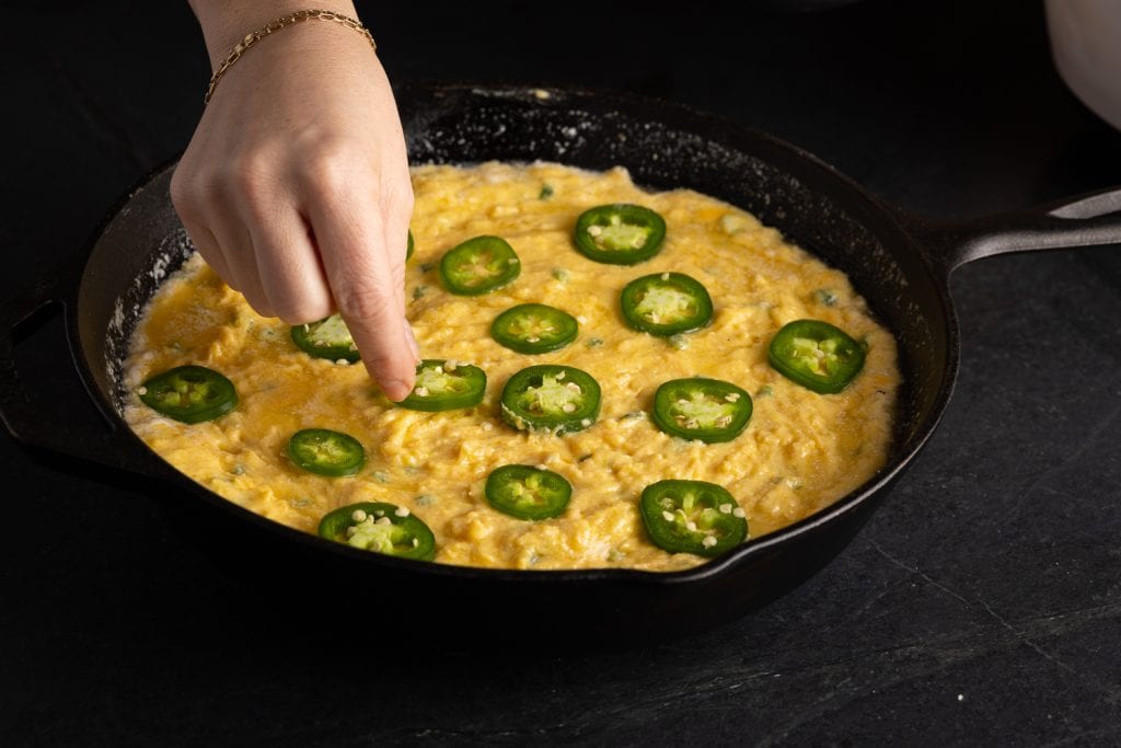 Sliced jalapenos being added to the top of cornbread batter.