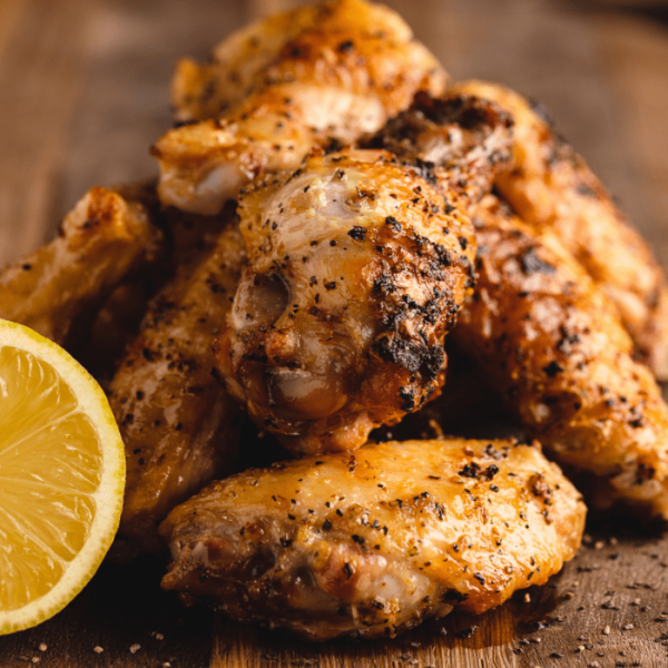 Grilled lemon pepper wings stacked on a wooden cutting board.