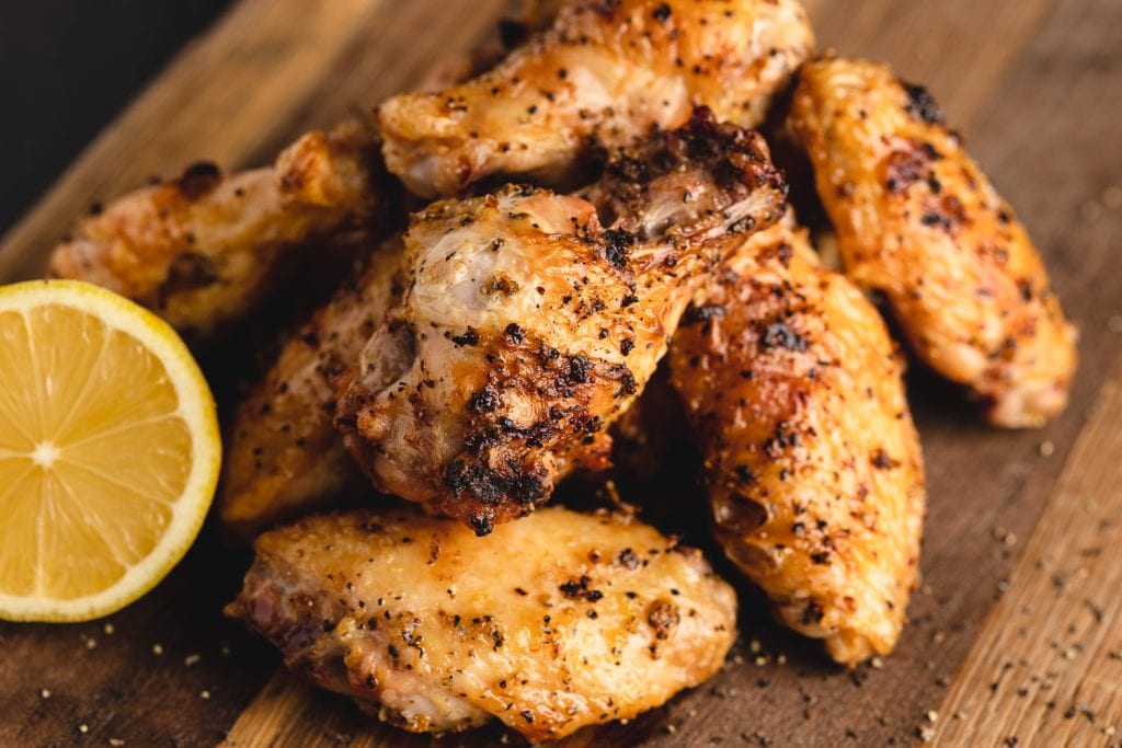 Grilled lemon pepper wings stacked on a wooden cutting board.