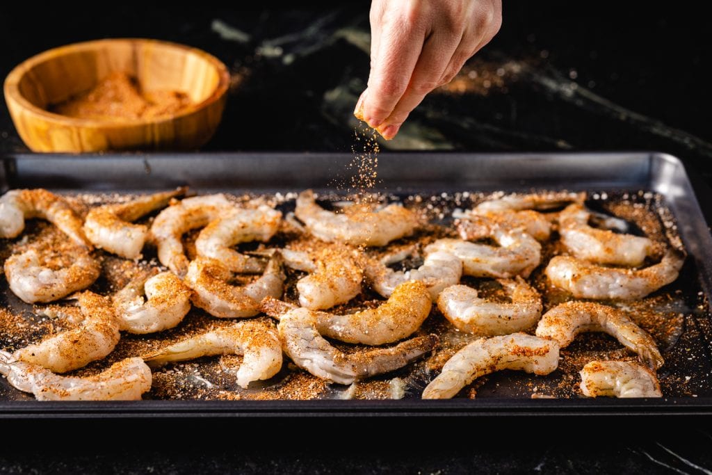 Cajun seasoning being sprinkled on a baking sheet full of shrimp.