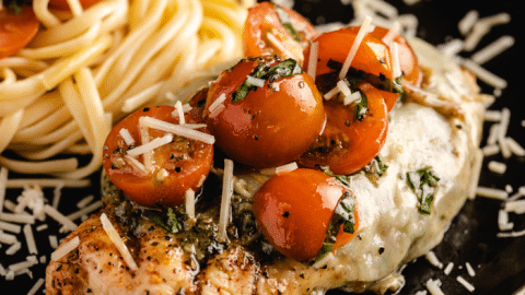 Grilled chicken margherita on a serving dish next to pasta.