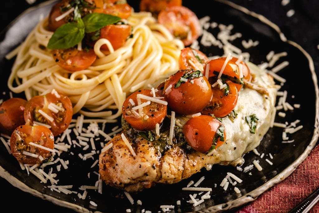Grilled chicken margherita on a serving dish next to pasta.