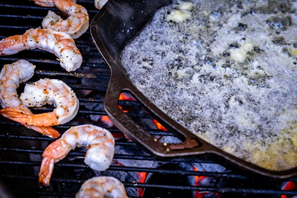 Shrimp on the BBQ next to a skillet of melted butter.