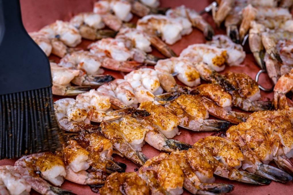 Shrimp on skewers being seasoned with cajun seasoning.