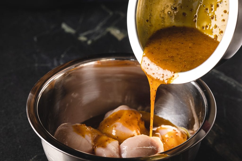 Honey mustard marinade being poured over a bowl of chicken breasts.